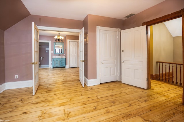 unfurnished bedroom featuring vaulted ceiling, an inviting chandelier, and light hardwood / wood-style floors