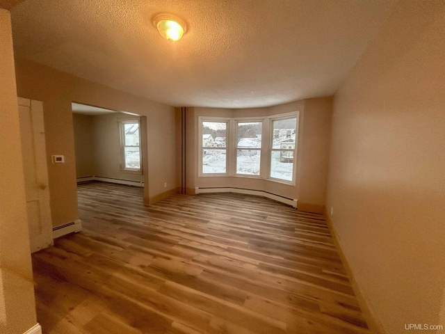 empty room featuring a textured ceiling, wood-type flooring, and baseboard heating