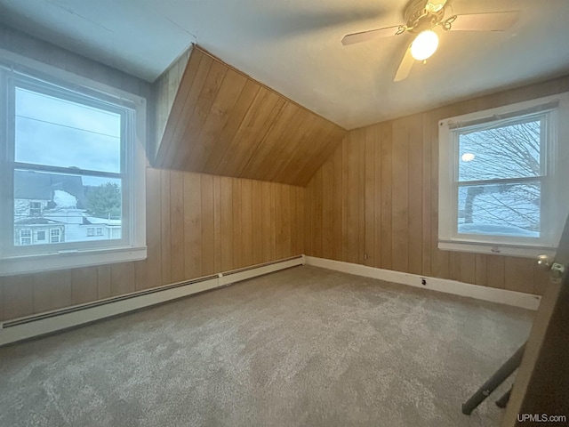 additional living space with wood walls, lofted ceiling, ceiling fan, baseboard heating, and carpet floors