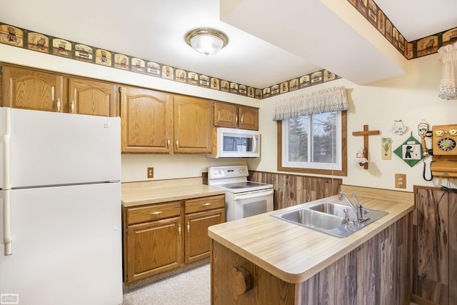 kitchen with kitchen peninsula, wood walls, sink, and white appliances