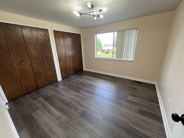 unfurnished bedroom with two closets, dark hardwood / wood-style floors, and an inviting chandelier