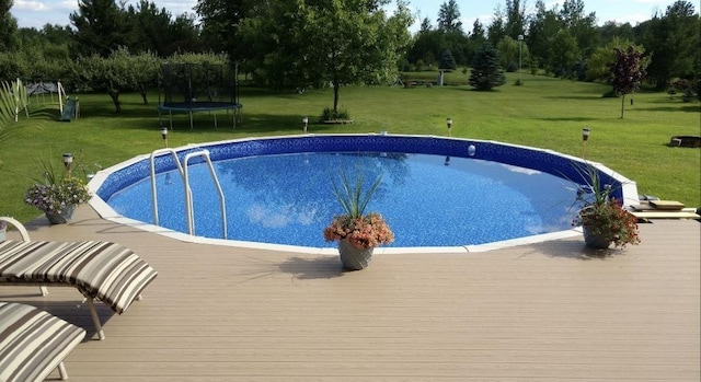 view of swimming pool featuring a trampoline, a deck, and a lawn