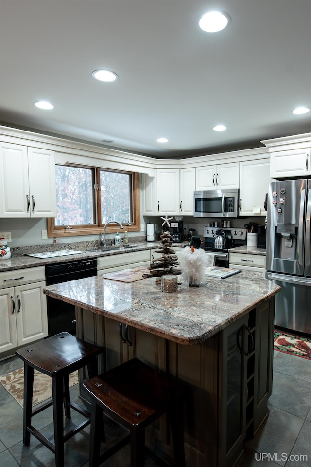 kitchen with white cabinets, stainless steel appliances, a kitchen island, and light stone counters