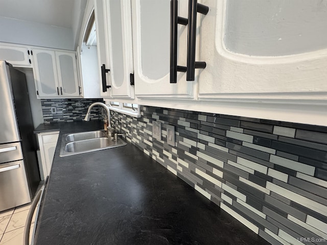 room details featuring white cabinets, backsplash, stainless steel refrigerator, and sink