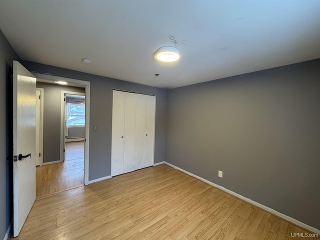 unfurnished bedroom with light wood-type flooring, baseboard heating, and a closet