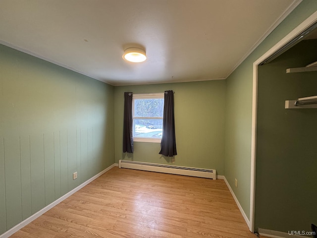 empty room with ornamental molding, light hardwood / wood-style floors, and a baseboard heating unit