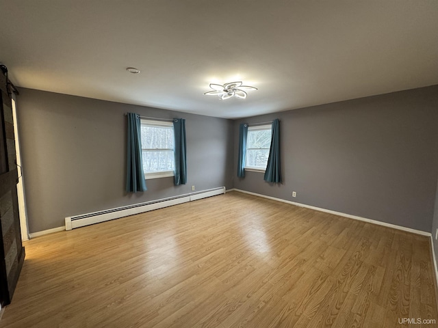 empty room featuring plenty of natural light, a fireplace, baseboard heating, and light hardwood / wood-style flooring