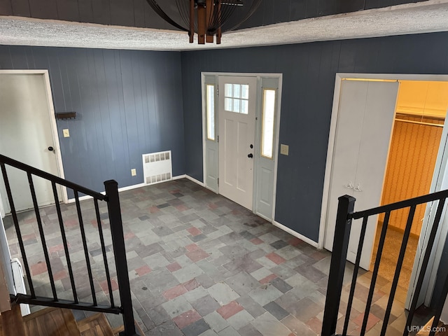 foyer entrance featuring radiator heating unit, a textured ceiling, and wood walls