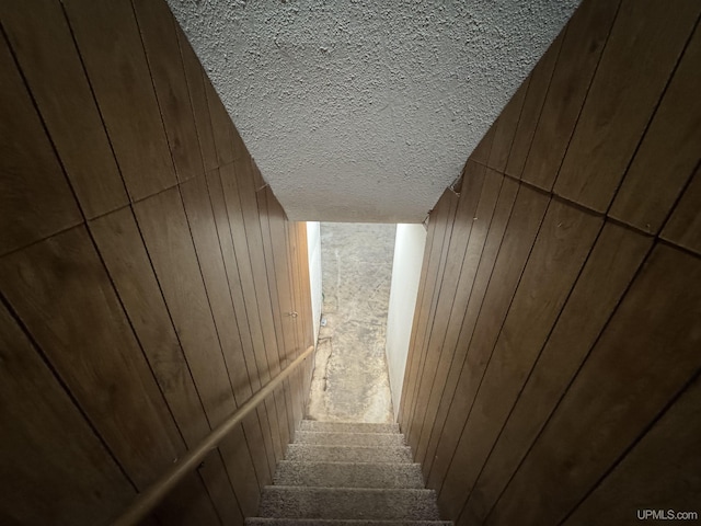 stairs with carpet flooring, a textured ceiling, and wooden walls