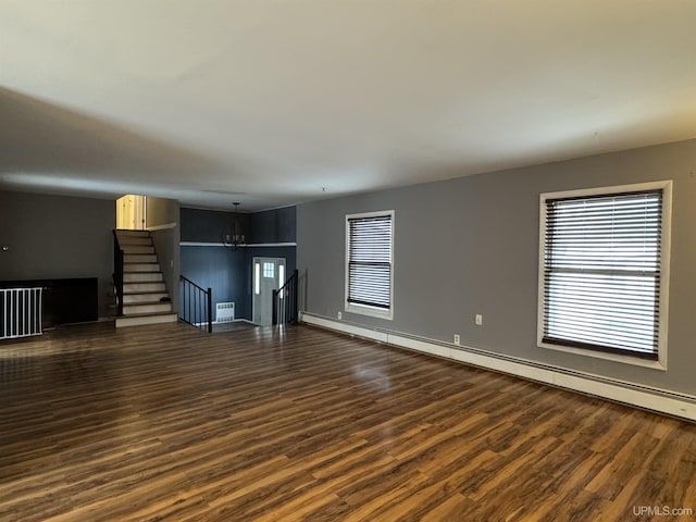 unfurnished living room with dark wood-type flooring, an inviting chandelier, baseboard heating, and a healthy amount of sunlight