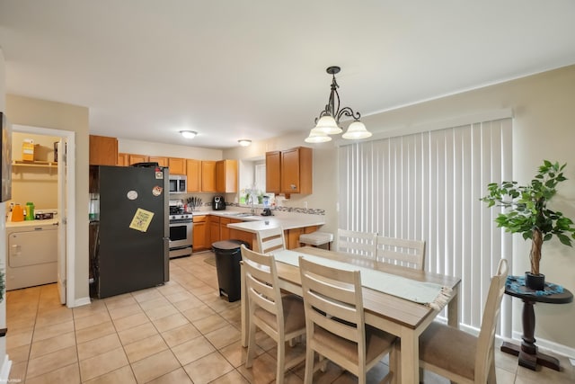 kitchen featuring sink, hanging light fixtures, appliances with stainless steel finishes, light tile patterned flooring, and washer / dryer