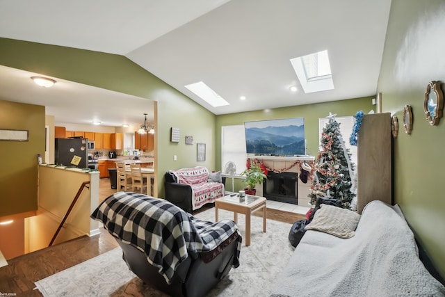 living room featuring a tile fireplace, an inviting chandelier, light hardwood / wood-style flooring, and lofted ceiling with skylight