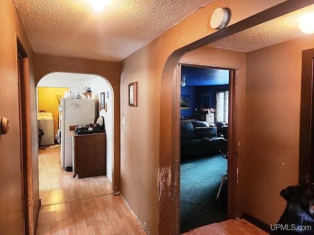 hall with washer / dryer, a textured ceiling, and light hardwood / wood-style flooring