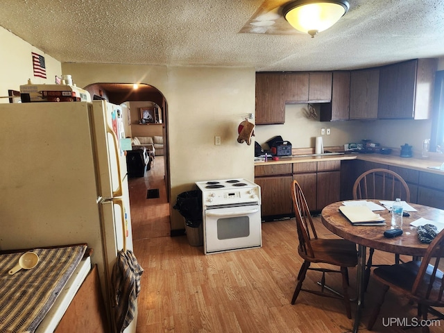 kitchen featuring a textured ceiling, dark brown cabinetry, white appliances, and light wood-type flooring