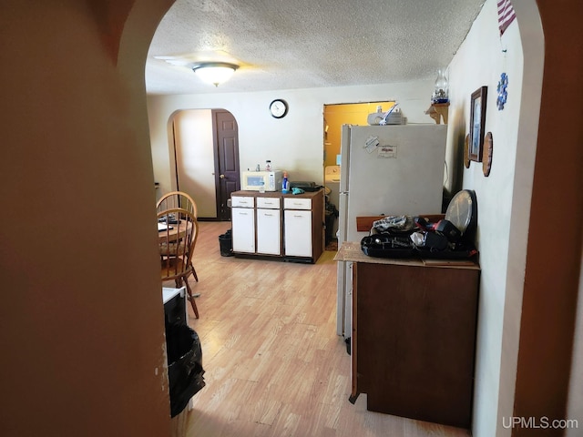 kitchen featuring white cabinetry, white appliances, a textured ceiling, and light hardwood / wood-style flooring