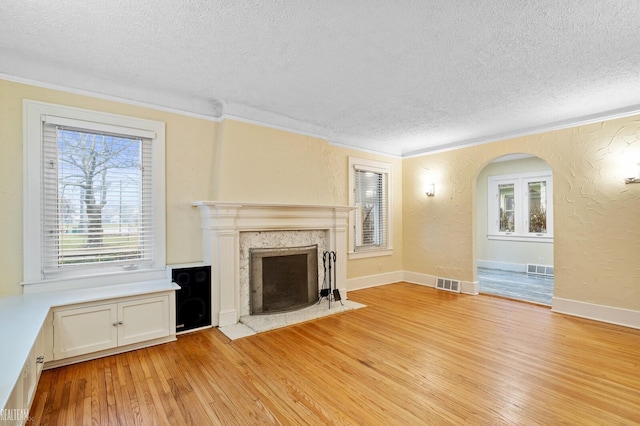 unfurnished living room with crown molding, a premium fireplace, a textured ceiling, and light hardwood / wood-style flooring