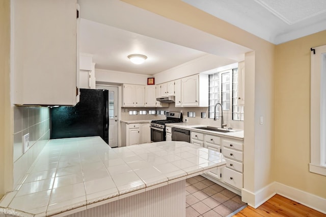 kitchen featuring sink, tile countertops, kitchen peninsula, light hardwood / wood-style floors, and appliances with stainless steel finishes