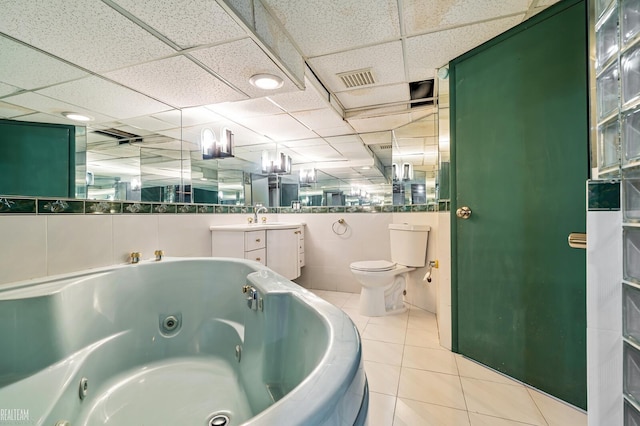 bathroom featuring tile patterned flooring, a washtub, a drop ceiling, and toilet