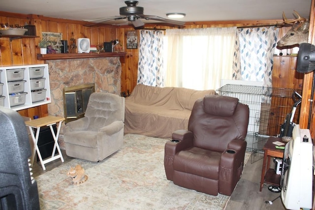 living room featuring ceiling fan, a stone fireplace, and wooden walls