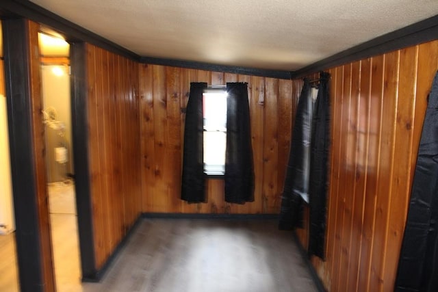 empty room with a textured ceiling, crown molding, and wooden walls