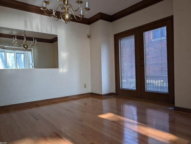 unfurnished room featuring hardwood / wood-style floors, a chandelier, ornamental molding, and french doors