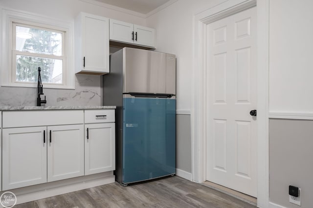 kitchen with light stone countertops, stainless steel fridge, backsplash, light wood-type flooring, and white cabinetry