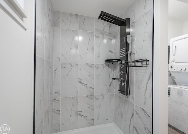 bathroom with stacked washer / dryer and tiled shower