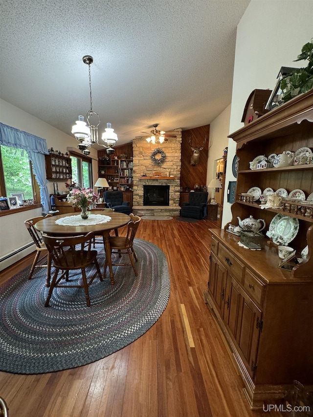 dining space featuring hardwood / wood-style floors, a textured ceiling, a stone fireplace, and vaulted ceiling