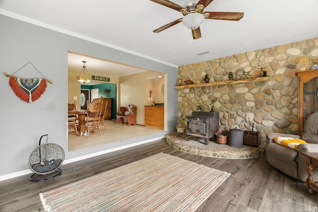 living room with hardwood / wood-style flooring, a wood stove, ceiling fan, and ornamental molding