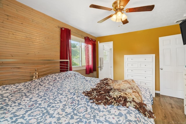 bedroom featuring hardwood / wood-style floors, ceiling fan, and wooden walls