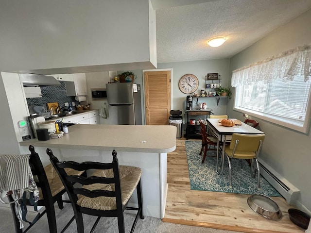 kitchen with a baseboard heating unit, white cabinets, a textured ceiling, kitchen peninsula, and stainless steel refrigerator