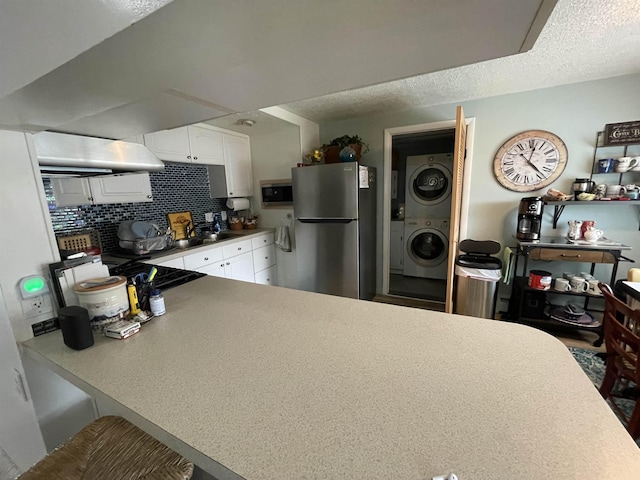 kitchen with range hood, backsplash, white cabinets, stacked washer and clothes dryer, and appliances with stainless steel finishes