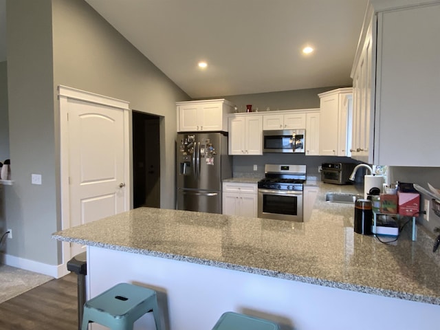 kitchen with white cabinets, appliances with stainless steel finishes, kitchen peninsula, and a kitchen breakfast bar