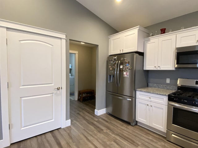 kitchen with light stone countertops, appliances with stainless steel finishes, hardwood / wood-style flooring, white cabinetry, and lofted ceiling