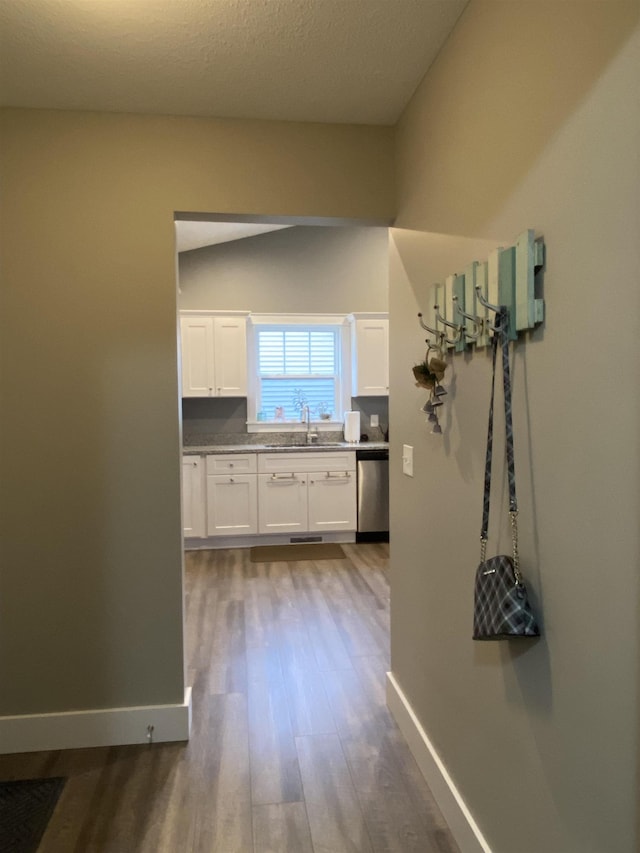 corridor featuring a textured ceiling, wood-type flooring, sink, and vaulted ceiling