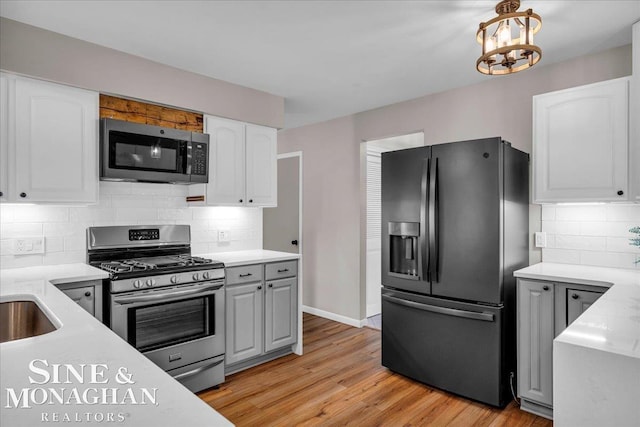 kitchen with decorative backsplash, stainless steel appliances, a notable chandelier, light hardwood / wood-style floors, and white cabinetry