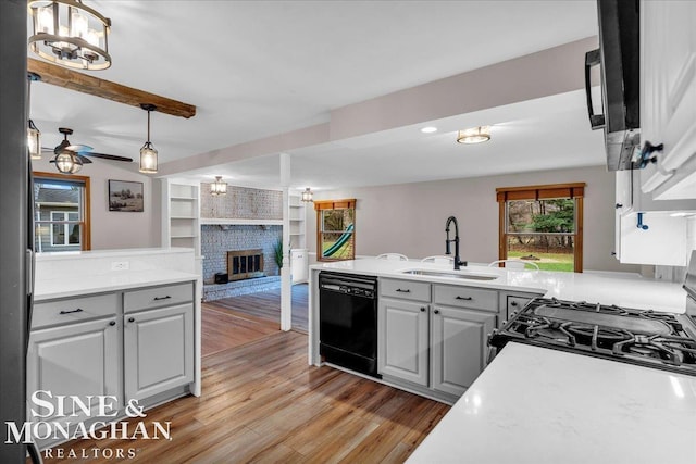 kitchen with sink, hanging light fixtures, ceiling fan, a fireplace, and black dishwasher