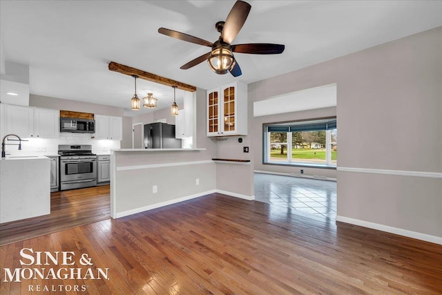 kitchen with kitchen peninsula, backsplash, black fridge, stainless steel range oven, and white cabinetry