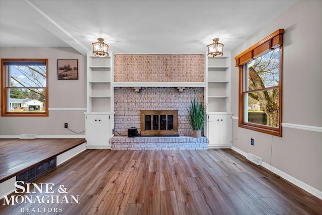 unfurnished living room with hardwood / wood-style floors, an inviting chandelier, and a brick fireplace