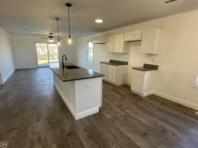 kitchen featuring ceiling fan, sink, white cabinets, hanging light fixtures, and an island with sink