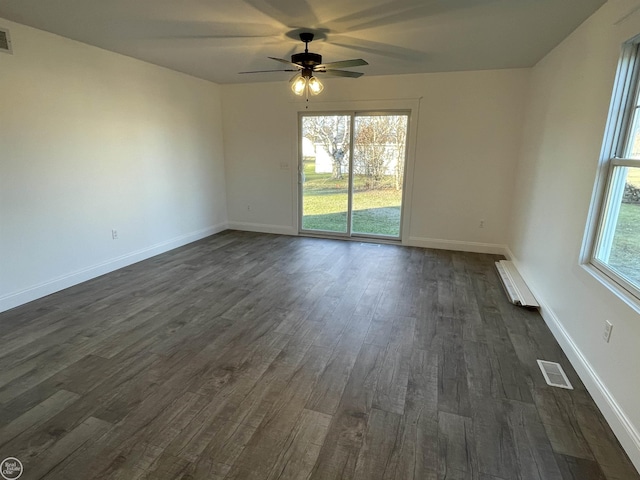 spare room featuring a wealth of natural light, dark hardwood / wood-style flooring, ceiling fan, and a baseboard heating unit