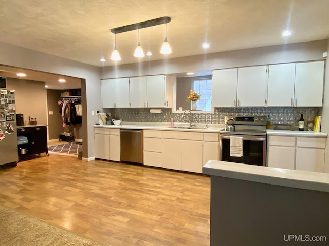 kitchen featuring appliances with stainless steel finishes, light wood-type flooring, sink, decorative light fixtures, and white cabinetry