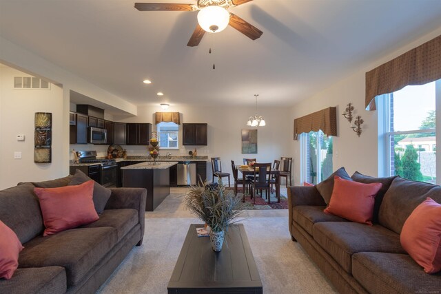 carpeted living room with ceiling fan with notable chandelier