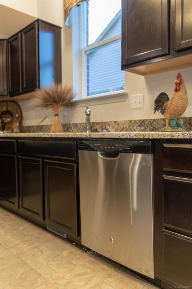 kitchen featuring stainless steel dishwasher, dark brown cabinetry, and dark stone counters