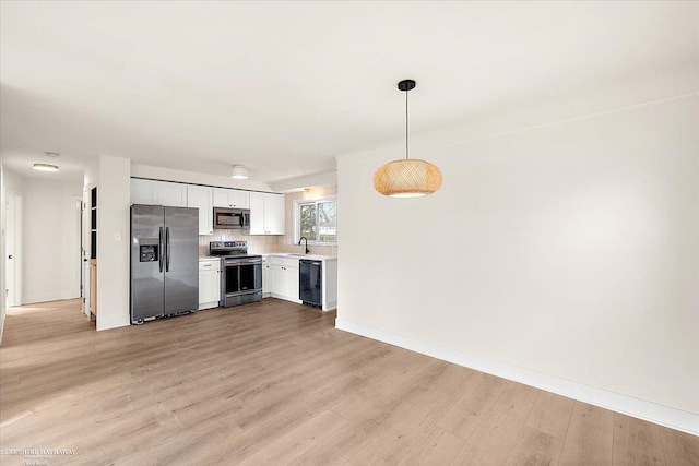 kitchen with white cabinets, decorative light fixtures, light wood-type flooring, and stainless steel appliances