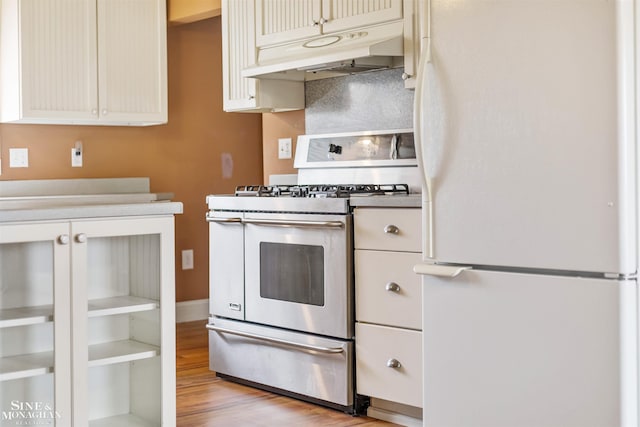 kitchen featuring cream cabinets, white refrigerator, light hardwood / wood-style floors, and stainless steel gas range oven