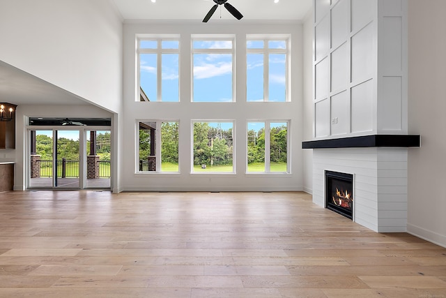 unfurnished living room with a large fireplace, light wood-type flooring, ceiling fan, and a towering ceiling