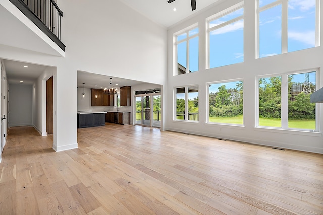 unfurnished living room with ceiling fan with notable chandelier, a high ceiling, and light hardwood / wood-style floors