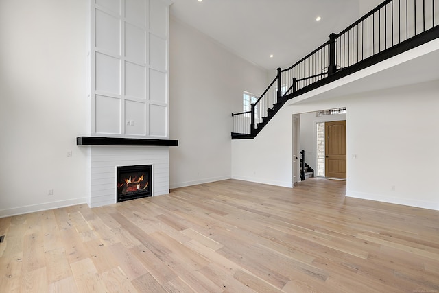 unfurnished living room featuring light hardwood / wood-style floors, a large fireplace, and a towering ceiling