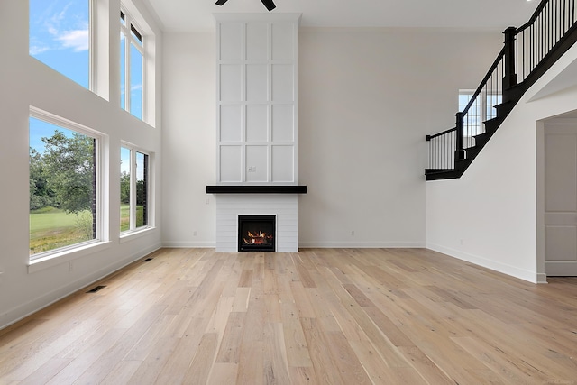 unfurnished living room with ceiling fan, light wood-type flooring, ornamental molding, and a fireplace